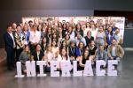 A large group photo of INTERLACE conference participants, smiling and gathered around the letters spelling 'INTERLACE', with posters visible in the background.